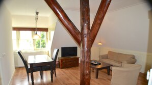 A living room with a wooden ceiling beam, a dining table with chairs, a sofa, and a television. - Appartementenboerderij Nieuwesluis (Wieringerwaard)