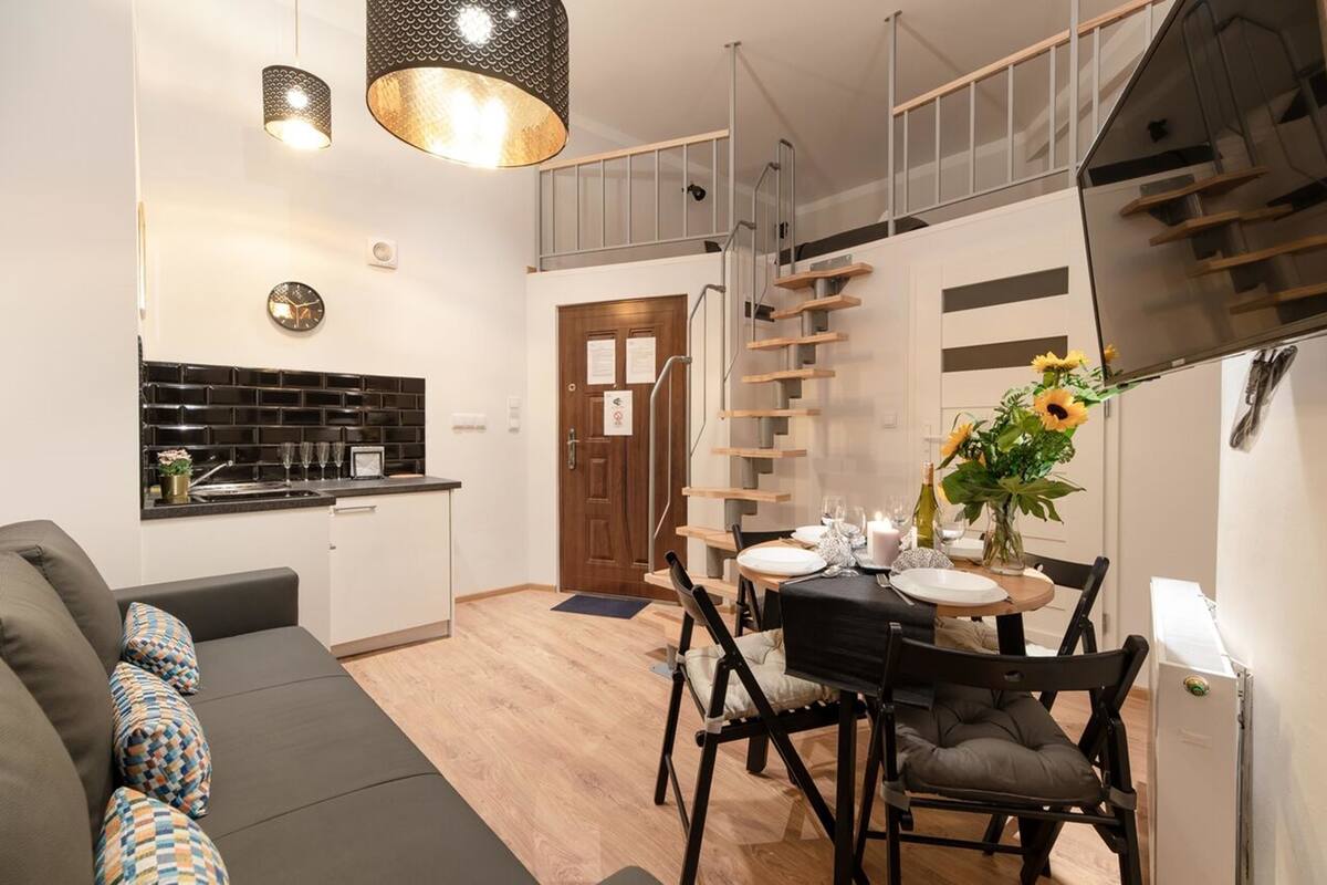A compact living space with a kitchenette, a dining area, and a staircase leading to an upper level.