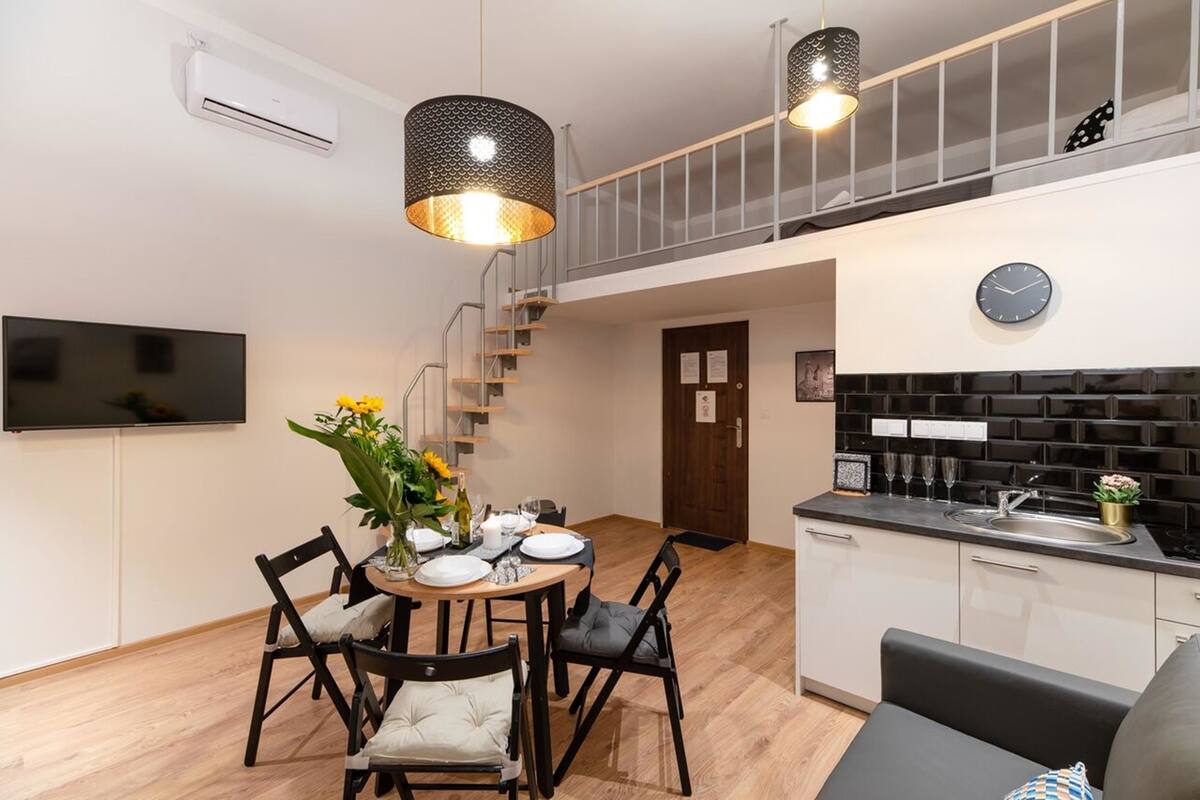 A modern kitchen with a black backsplash, a dining area with a round table and chairs, and a staircase leading to an upper level.