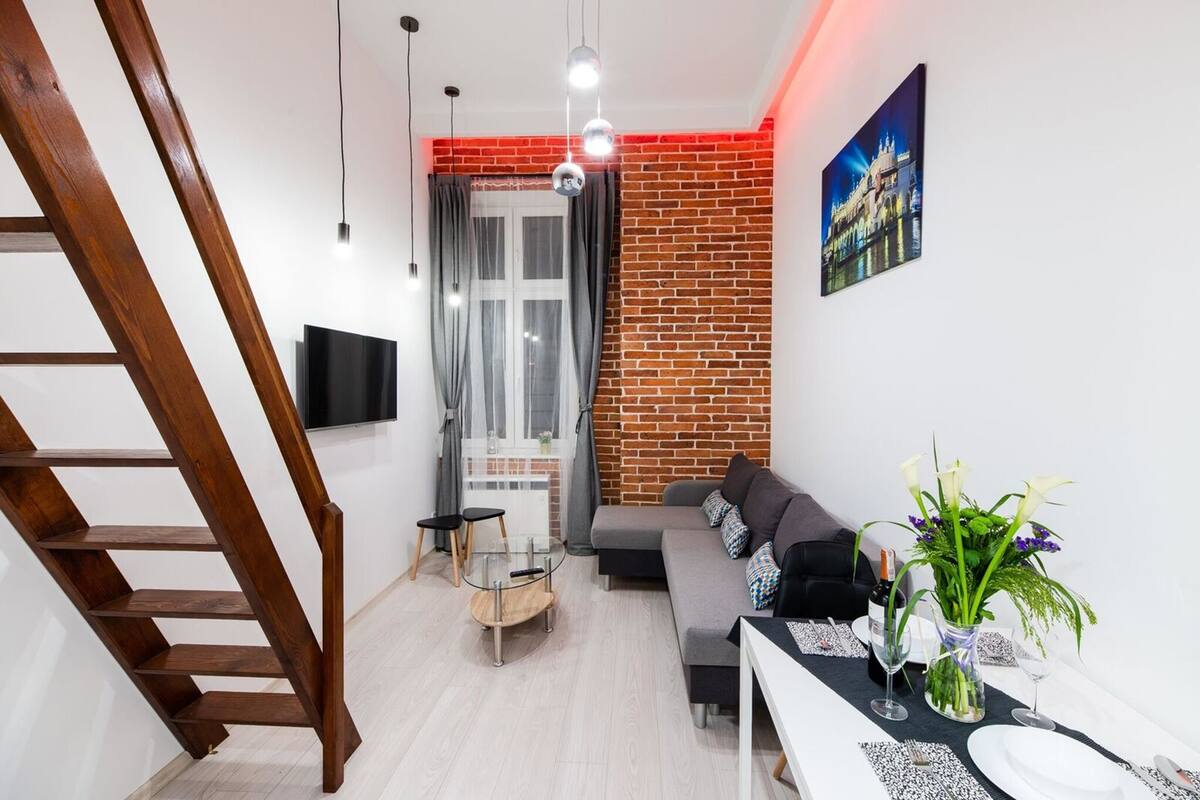 A modern living room with a wooden staircase, a grey sofa, a glass coffee table, and a brick accent wall.
