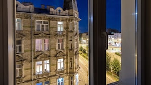 Vista de un edificio de varios pisos con detalles arquitectónicos ornamentales y grandes ventanales, tomada desde el interior de una habitación a través de una ventana.