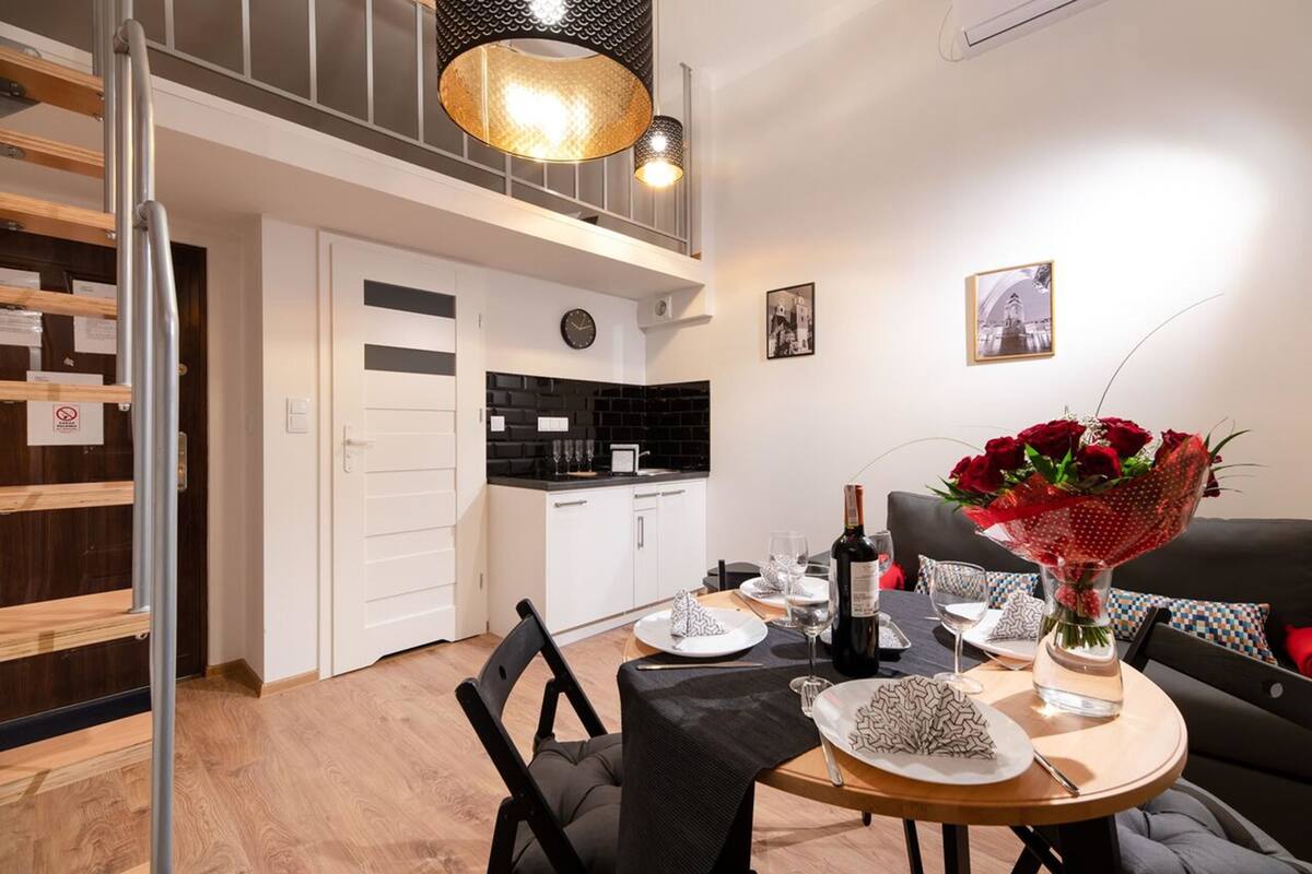 A modern kitchen with white cabinets and a black countertop, a dining area with a round table, and a sofa with a red cushion.