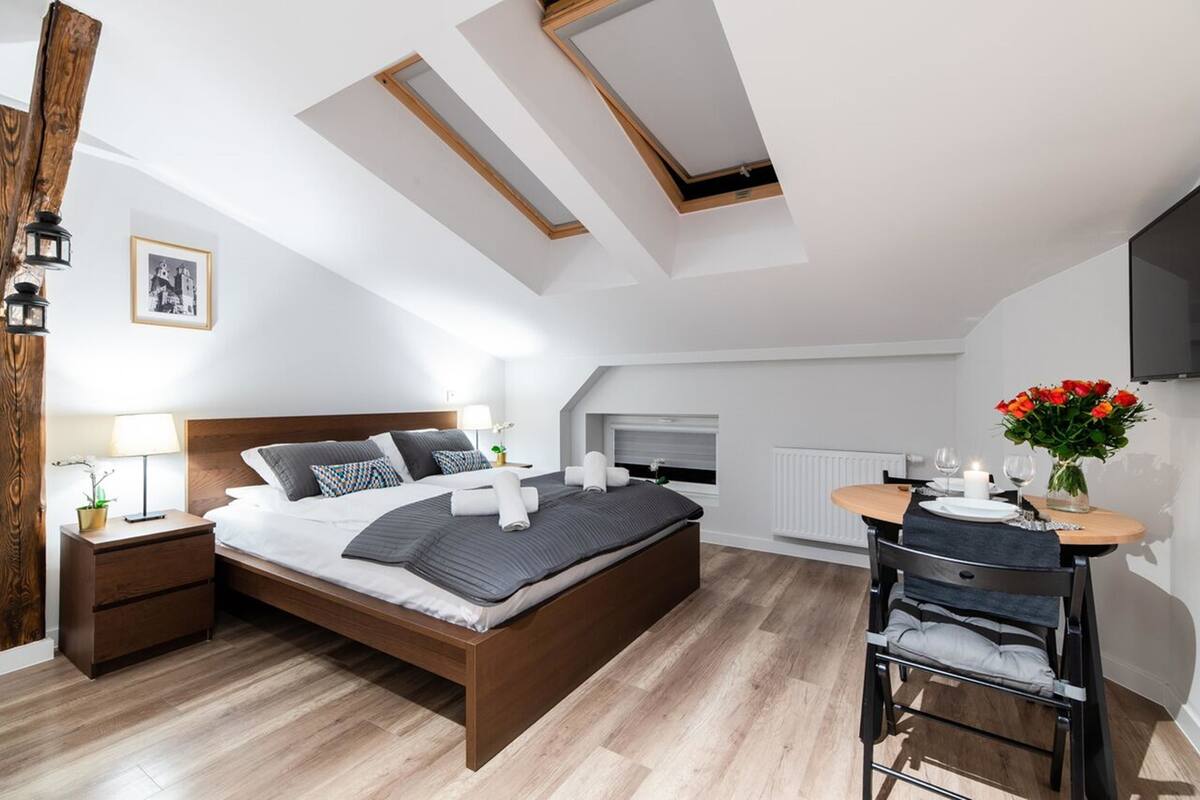 A modern bedroom with a large bed, a small table with a vase of flowers, and a ceiling with skylights.