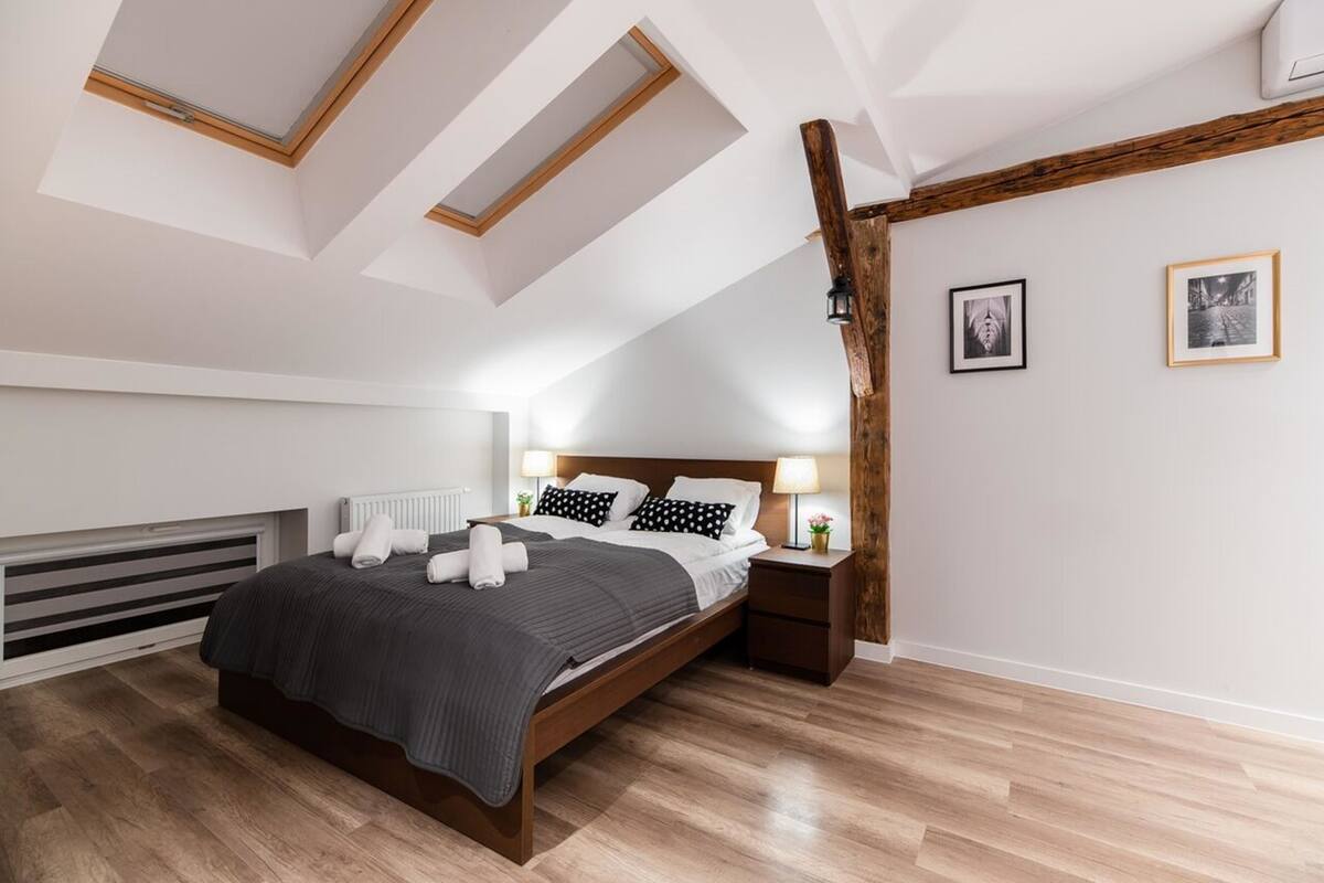A modern bedroom with a sloped ceiling, a wooden bed frame, a radiator, and a nightstand with a lamp.