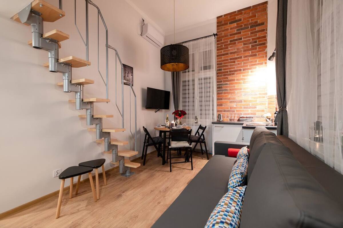 A compact living space with a staircase, a dining area, a sofa, and a kitchen.