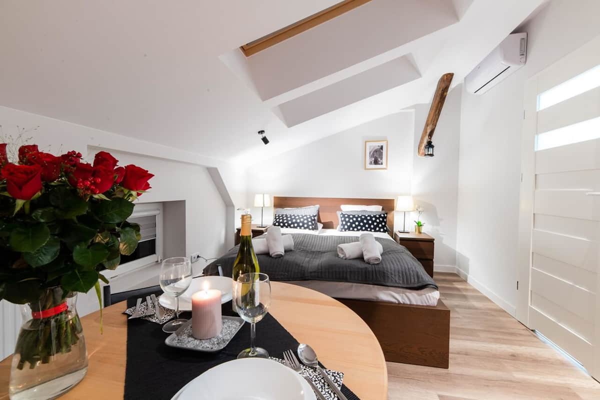 A modern bedroom with a skylight, a neatly made bed, and a dining area set with a candle and wine.