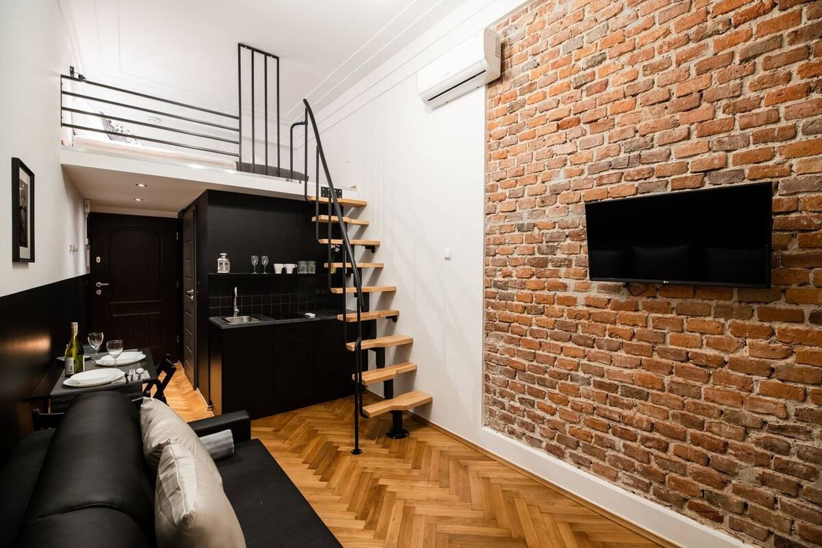 A compact living space with a kitchen, dining area, and a staircase leading to a loft.