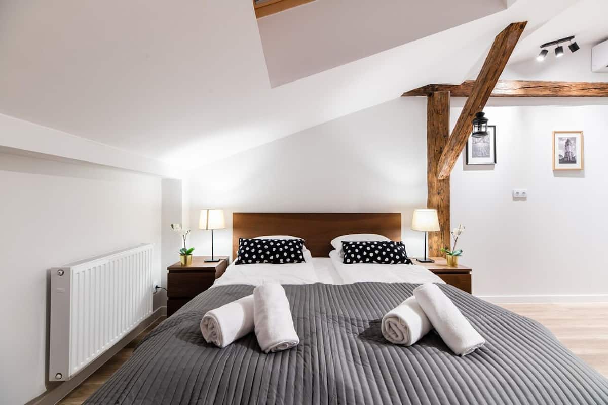 A neatly made bed with rolled towels, a wooden headboard, and a white radiator.