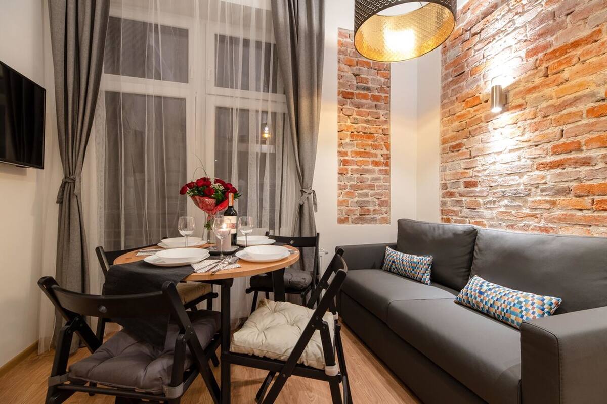 A modern living room with a brick wall, a black leather sofa, and a dining table set for two.
