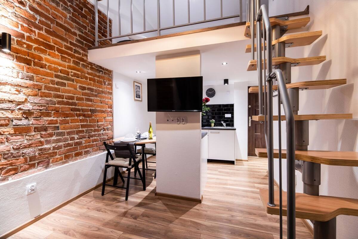 A modern interior with exposed brick walls, a dining area, a kitchen, and a staircase.