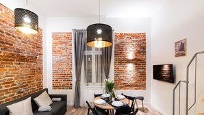 Una sala moderna con pared de ladrillo, un sofá negro, una mesa de comedor con sillas y una escalera.