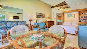 A cozy room with a round glass table, wicker chairs, a sofa, a bed, and a bookshelf. - Maui Kaanapali S #e290 Studio Bedroom Condo by RedAwning (Lahaina)