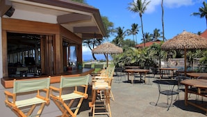 An outdoor seating area with wooden tables and chairs, a bar, and thatched umbrellas. - Maui Kaanapali S #e290 Studio Bedroom Condo by RedAwning (Lahaina)