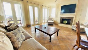 A spacious living room with a sofa, armchair, and coffee table. There is a fireplace and a television mounted on the wall. - Portofino - Private Beachfront House 3 Bedroom Home by RedAwning (South Padre Island)