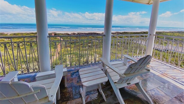 A covered outdoor seating area with white chairs and a view of the beach and ocean. - Portofino - Private Beachfront House 3 Bedroom Home by RedAwning (South Padre Island)