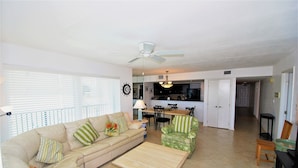 A living room with a beige sofa, a wooden coffee table, a green armchair, and a dining area with a table and chairs. - Seville Unit #201 3 Bedroom Condo by RedAwning (South Padre Island)
