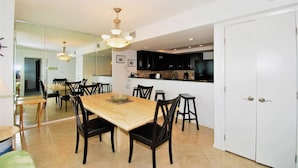 A dining area with a wooden table and chairs, a chandelier, and a kitchen in the background. - Seville Unit #201 3 Bedroom Condo by RedAwning (South Padre Island)