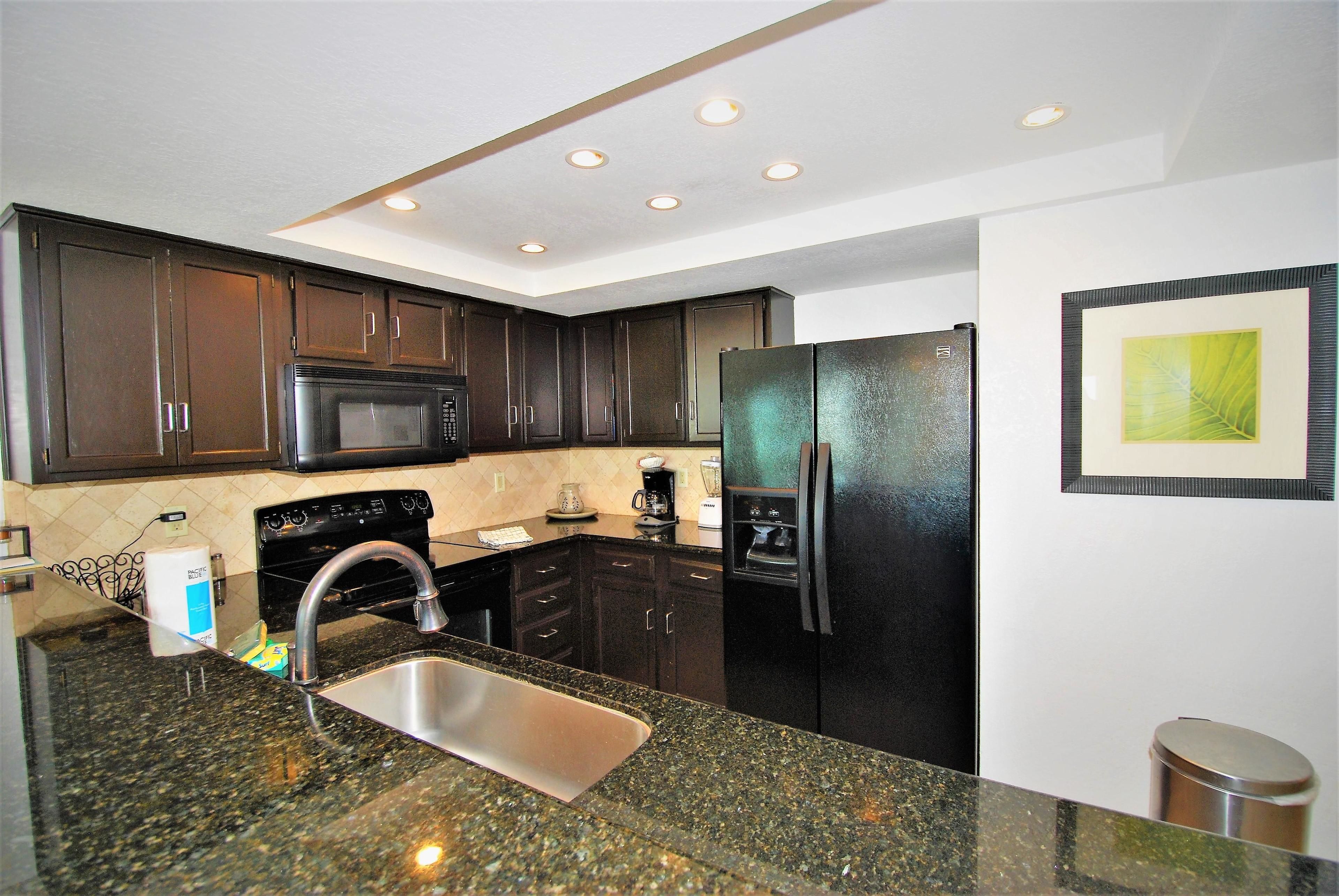 A kitchen with dark wooden cabinets, a stainless steel sink, a black refrigerator, and a microwave.