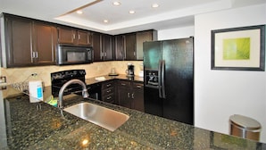 A kitchen with dark wooden cabinets, a stainless steel sink, a black refrigerator, and a microwave. - Seville Unit #201 3 Bedroom Condo by RedAwning (South Padre Island)