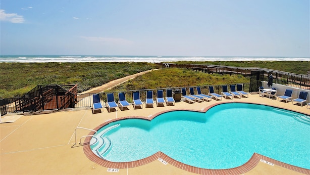 A swimming pool with a wooden deck, lounge chairs, and a view of the ocean. - Seville Unit #201 3 Bedroom Condo by RedAwning (South Padre Island)