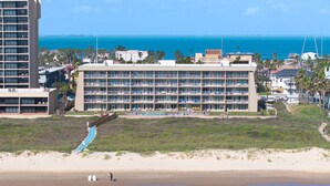 A beachfront hotel with multiple balconies, a pool, and a beach access ramp.