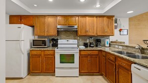 A kitchen with wooden cabinets, a white refrigerator, a microwave, a stove, and a sink.
