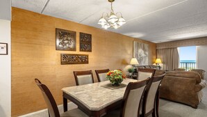 A dining area with a marble table, wooden chairs, and a chandelier. There is a sofa and a lamp in the background.