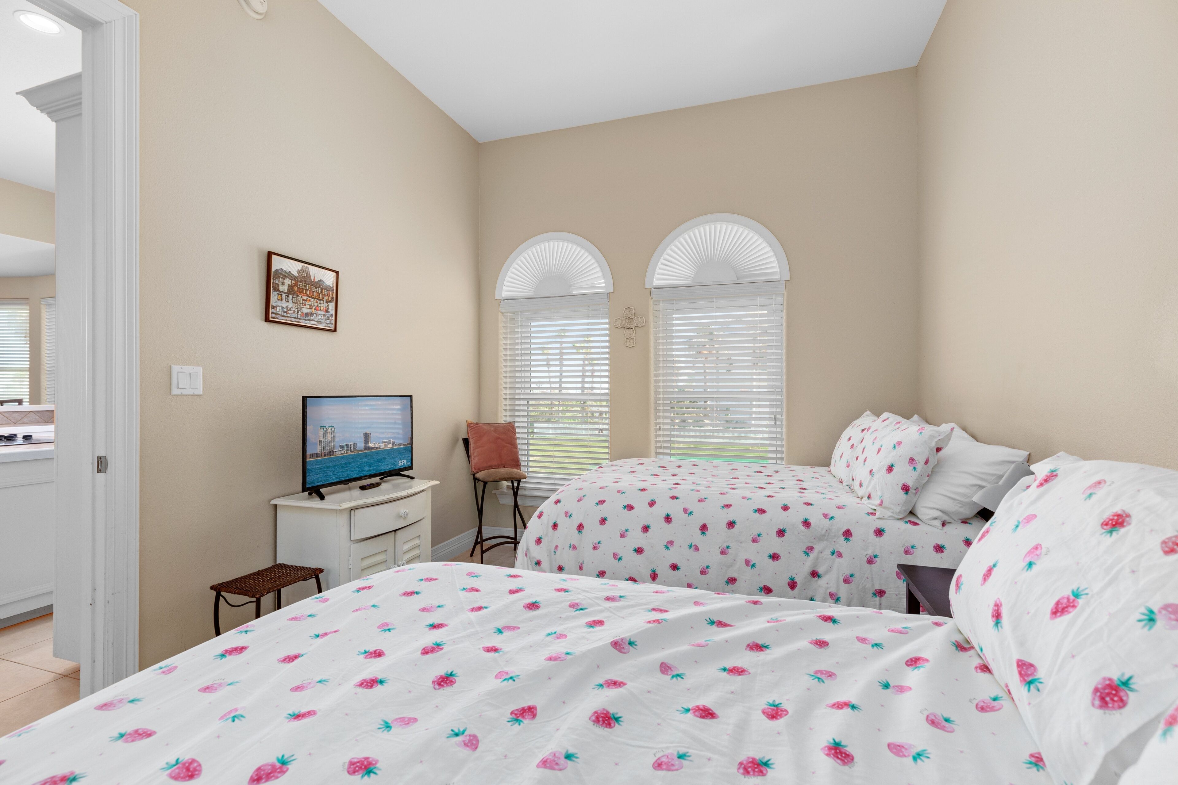 A bedroom with two beds, a TV, and a small desk.