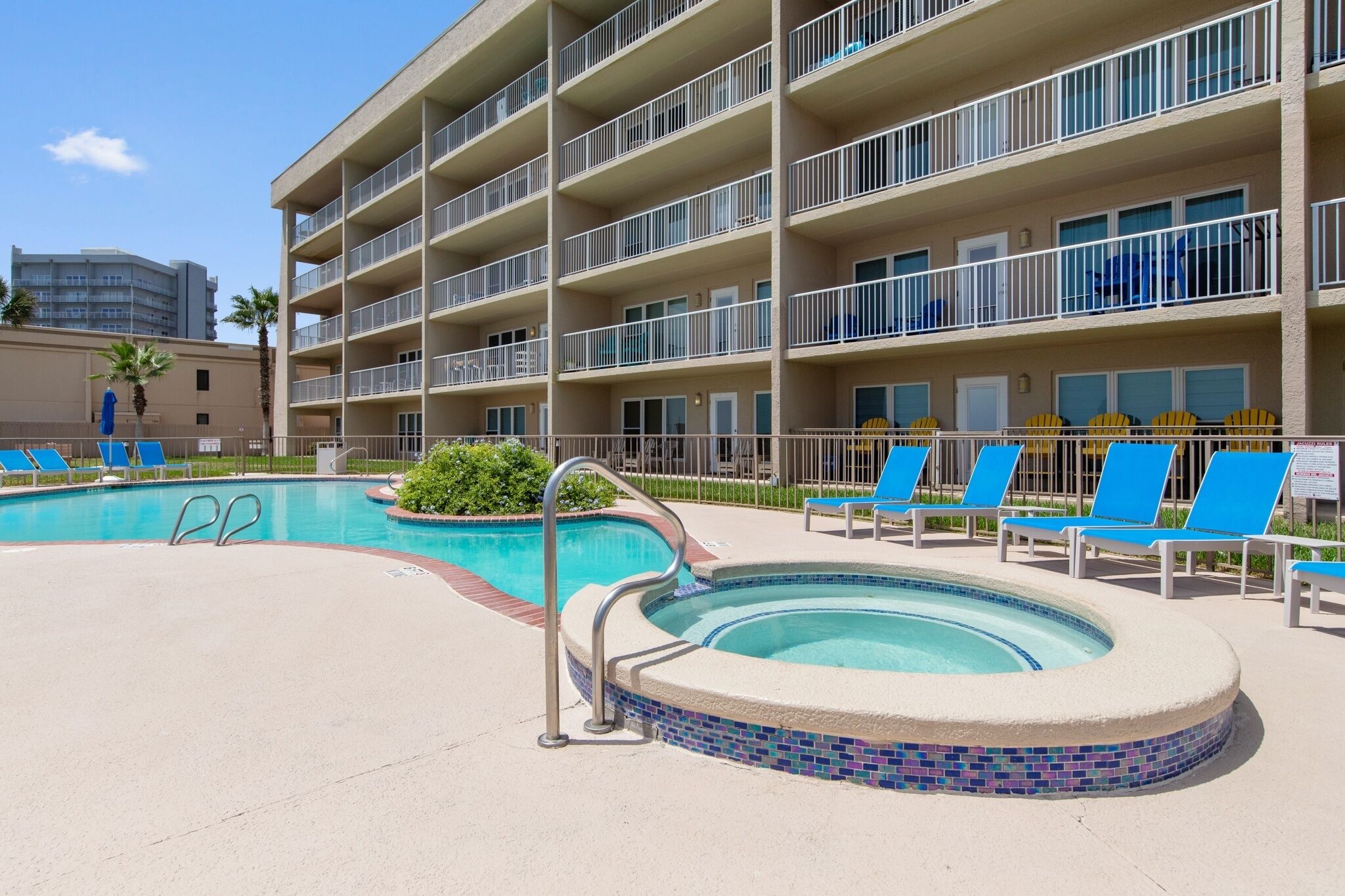 A hotel with a swimming pool, lounge chairs, and a multi-story building.