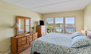 A bedroom with a bed, dresser, mirror, and a TV.