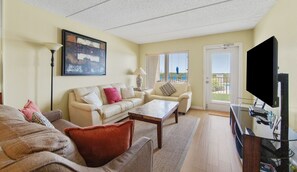 Ein Wohnzimmer mit einer Couch, Sesseln, einem Couchtisch, einem Fernseher und einem Bild an der Wand.