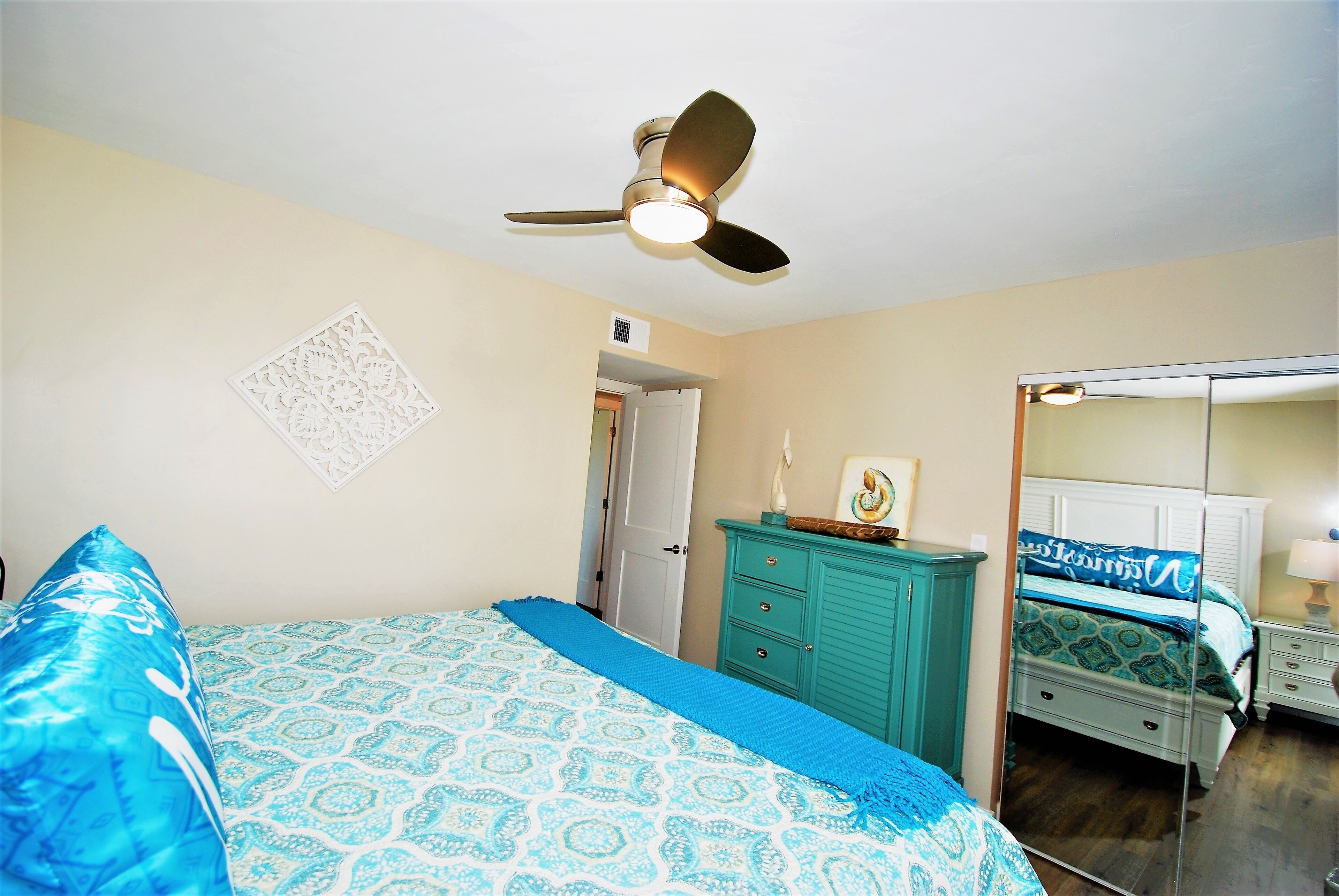 Une chambre à coucher avec un lit, un ventilateur de plafond, une commode et un miroir.
