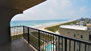 A balcony with a view of a beach, a swimming pool, and adjacent buildings. - Ocean Vista Unit #1201 3 Bedroom Condo by RedAwning (South Padre Island)