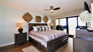 A bedroom with a bed, nightstands, a ceiling fan, and a view of the outside. - Ocean Vista Unit #1201 3 Bedroom Condo by RedAwning (South Padre Island)