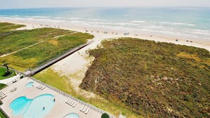 An aerial view of a beach resort with a swimming pool, beach umbrellas, and a walking path. - Ocean Vista Unit #1201 3 Bedroom Condo by RedAwning (South Padre Island)
