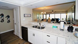 A kitchen with white cabinets, a double sink, and a marble countertop. - Ocean Vista Unit #1201 3 Bedroom Condo by RedAwning (South Padre Island)