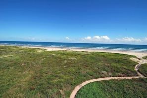 A coastal landscape with a beach, grassy areas, and a clear sky.