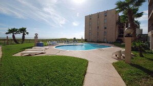Una piscina con sillones de descanso y un edificio al fondo.