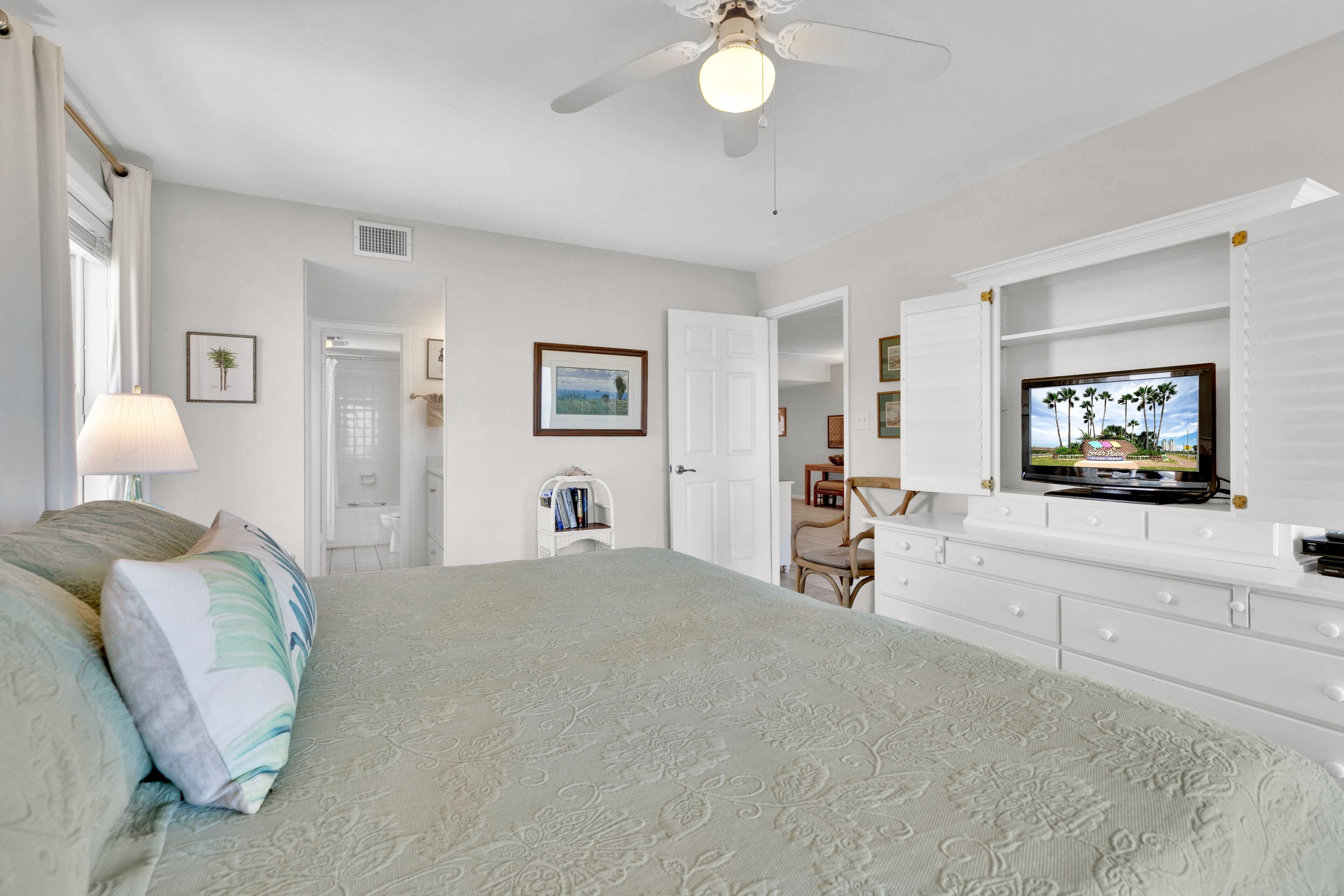 Un dormitorio con cama, televisor, cómoda y ventilador de techo.