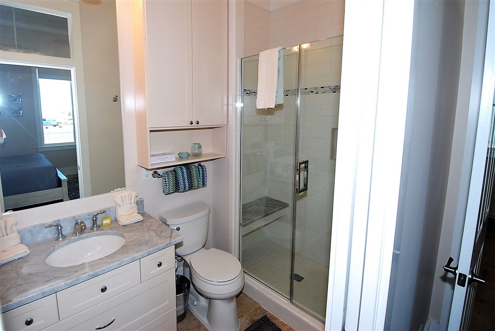 A bathroom with a glass-enclosed shower, a toilet, and a vanity with a sink and mirror.