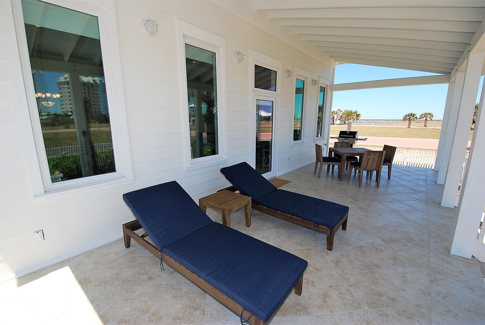 A covered outdoor area with two lounge chairs, a small table, and a grill.