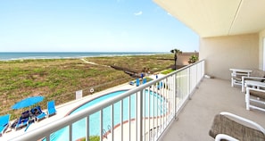 En balkong med pool, solstolar och utsikt över stranden och havet.