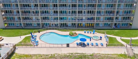 A multi-story hotel with a swimming pool, sun loungers, and a small garden area.