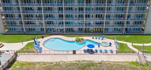 Un hôtel à plusieurs étages doté d’une piscine, de chaises longues et d’un petit jardin.