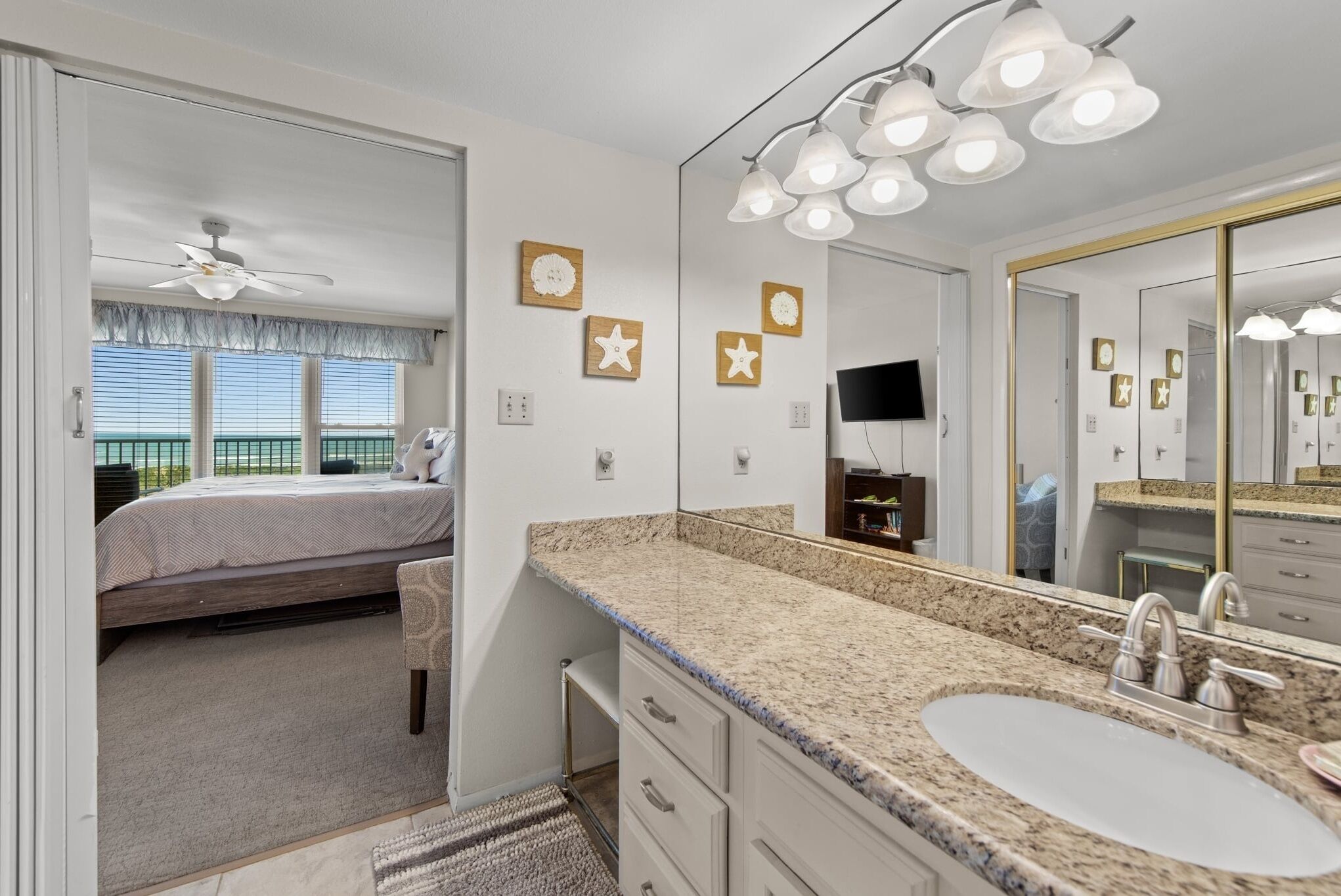 A bedroom with a bed, a bathroom with a sink, and a large mirror.