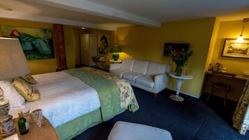 Habitación de hotel con cama, sofá, una mesita con lámpara, una silla y escritorio.