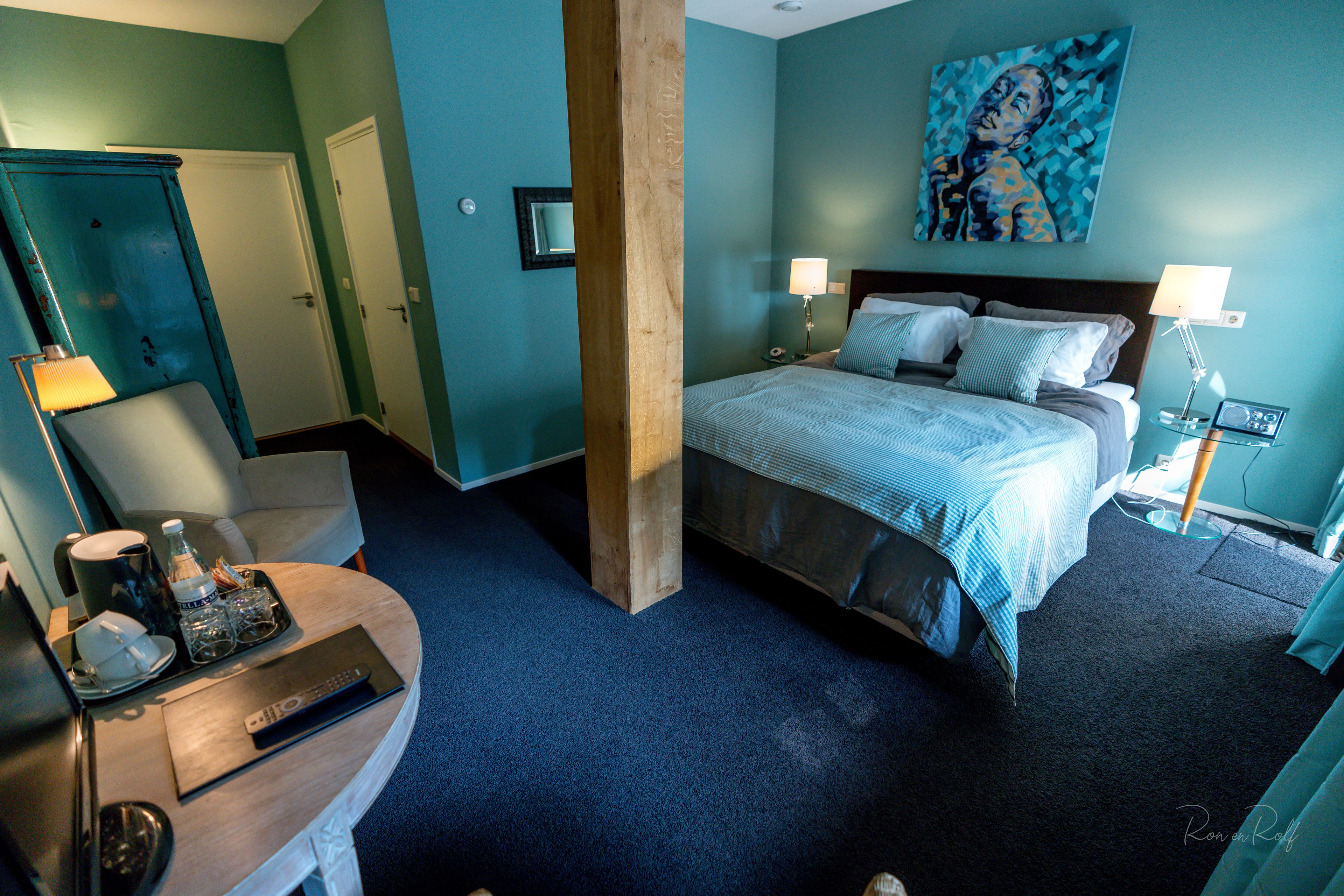 Una habitación de hotel con una cama, dos lámparas de noche, un escritorio con lámpara, una silla y un cuadro en la pared.