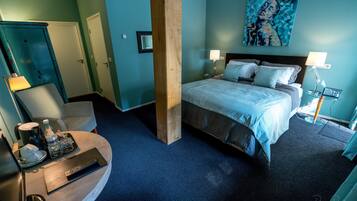 Una habitación de hotel con una cama, dos lámparas de noche, un escritorio con lámpara, una silla y un cuadro en la pared.