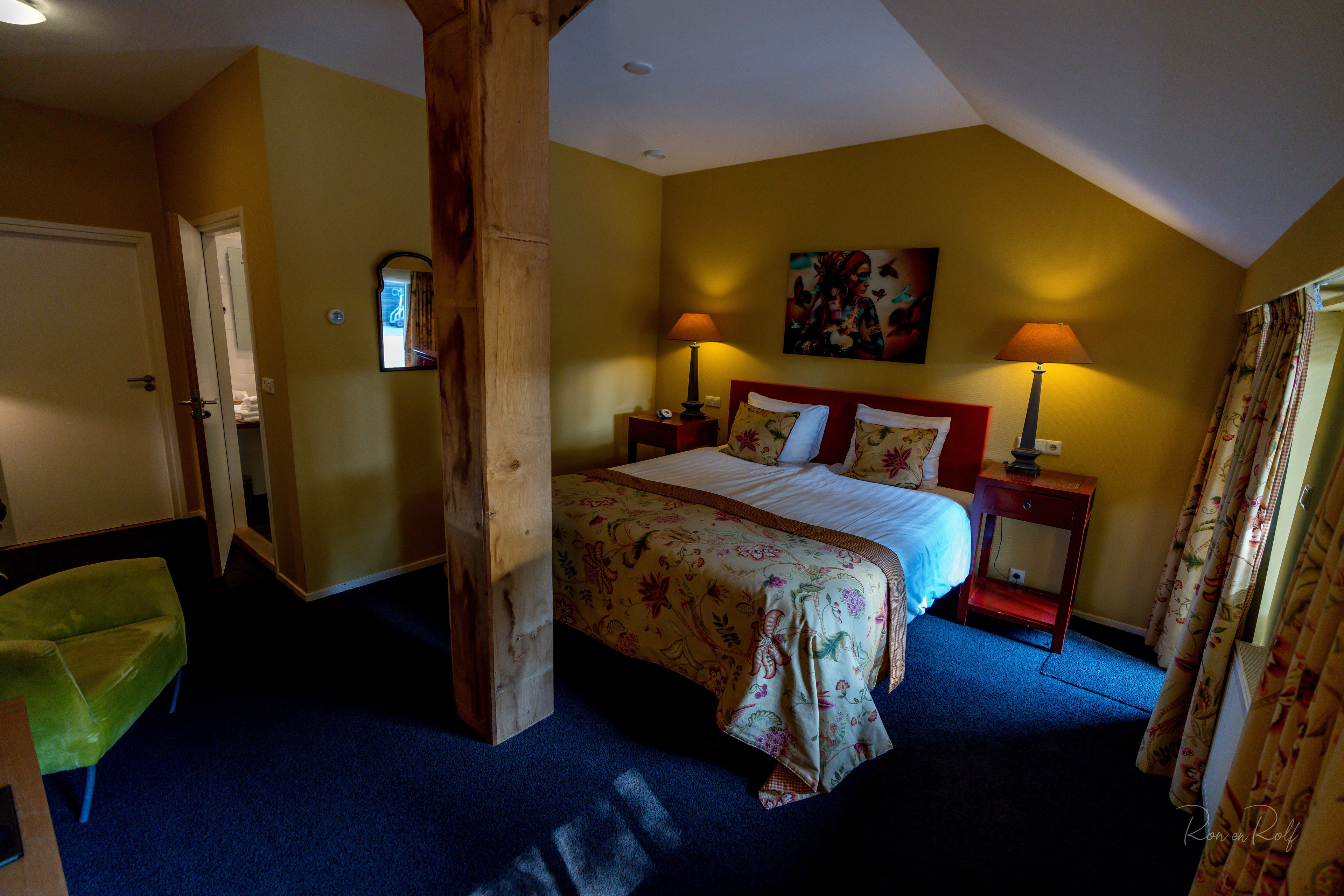 A bedroom with a bed, two bedside tables, a nightstand, a green chair, and a wooden beam structure.