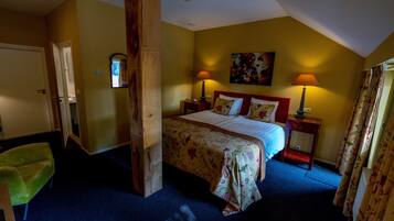 A bedroom with a bed, two bedside tables, a nightstand, a green chair, and a wooden beam structure.